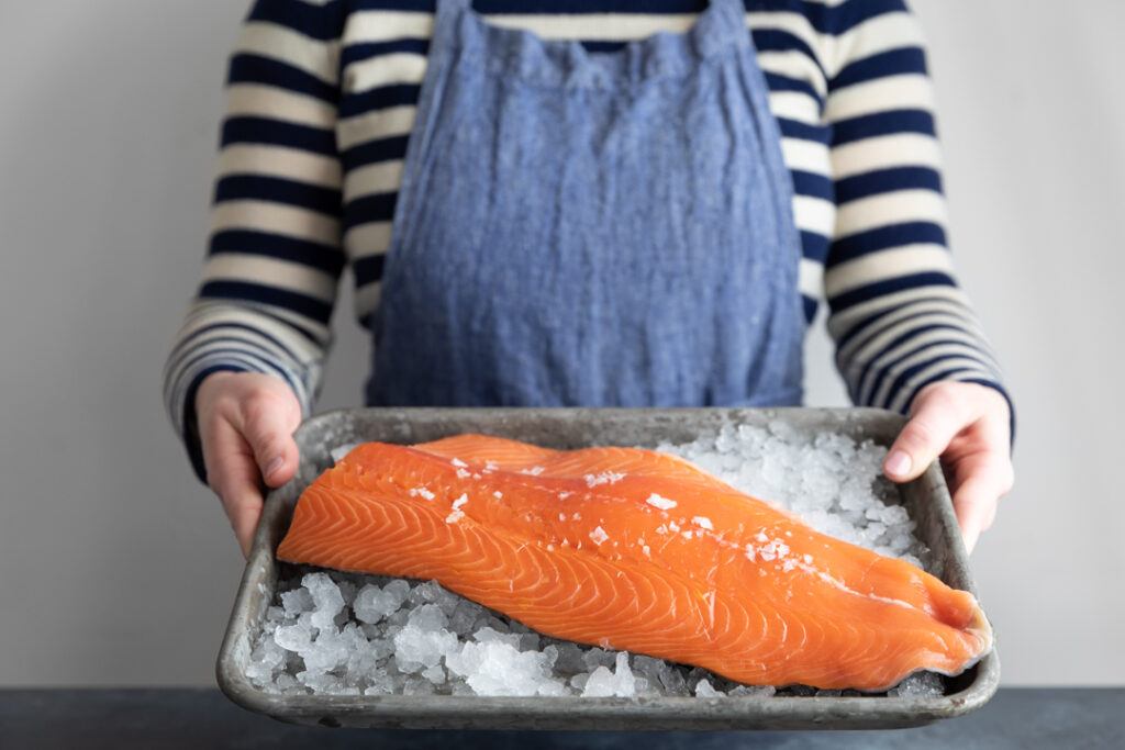Person Holds a Tray with Ice with Salmon on Top