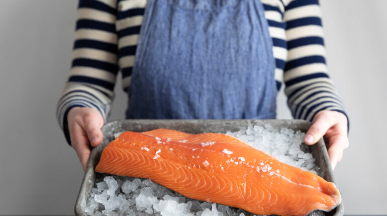 Person Holds a Tray with Ice with Salmon on Top
