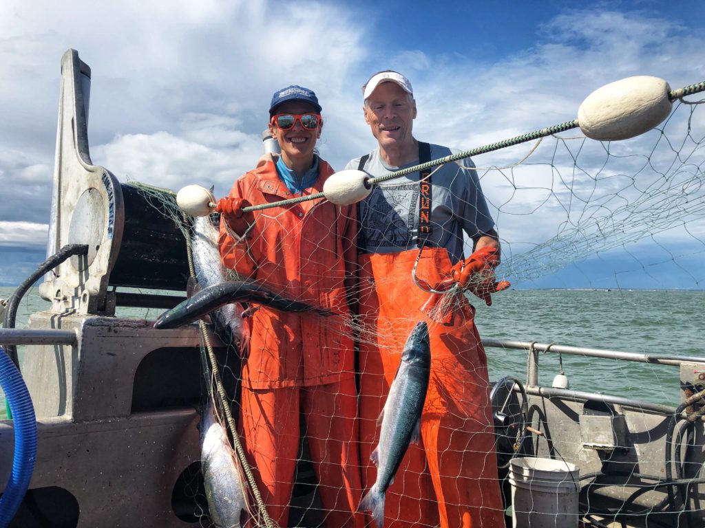 Two commercial salmon fishers on a boat at sea, holding up a net with salmon in it.