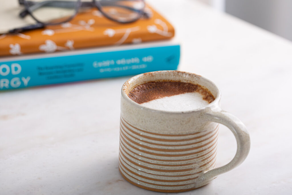 A Striped Mug of Elderberry Latte in Front of Two Journals and a Pair of Glasses