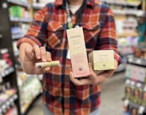 A person holds three body care products packaged in compostable cardboard up to the camera.