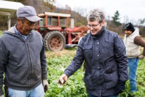 Farmer Andrea of Harmony Valley Farm with a Coworker Looking at a Black Radish