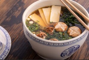 Bowl of Chanko Nabe with Two Chopsticks, Showing Slices of Tofu, Vegan Meatballs, and Mushrooms