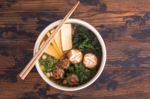 Chanko Nabe in a White Bowl with a Pair of Chopticks at the Top, Showing Mushrooms, Tofu, and Vegan Meatballs