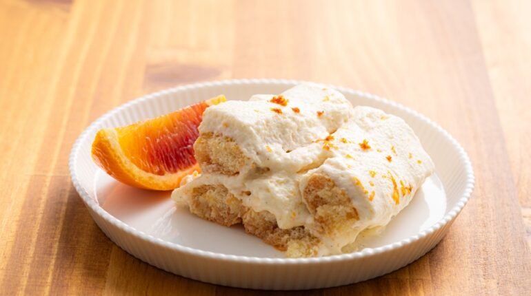 One Slice of Citrus Tiramisu on a White Plate with a Slice of Blood Orange