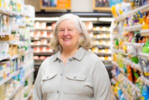 Woman in Gray Shirt Standing in Grocery Aisle Smiling