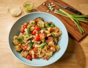 A Bowl Full of Panzanella Next to a Cutting Board with Green Onions