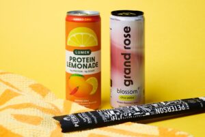 Protein Lemonade, Grand Rose Protein Drink, and a Beef Stick on a Yellow Background