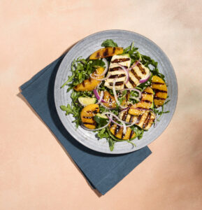 Grilled peach and halloumi salad on a plate with a blue napkin on the side