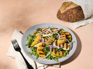 Grilled peach and halloumi salad on a plate with bread loaf on the side