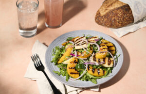 Grilled peach and halloumi salad on a plate with bread and drinks on the side