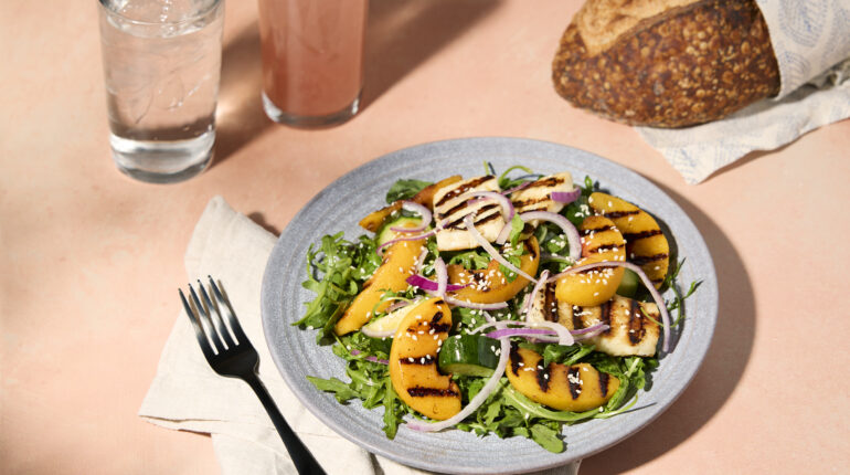 Grilled peach and halloumi salad on a plate with bread and drinks on the side