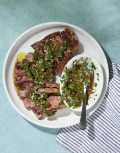 Sliced steak with chimichurri sauce on a plate with teal background