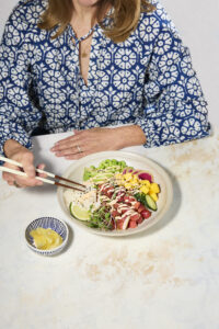 Person eating a poke bowl with chopsticks and ginger on the side