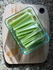 Celery sticks in a glass container on a wooden cutting board