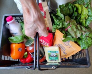 Looking Down Into a Grocery Basket with Greens, Coffee, Cheese, and More
