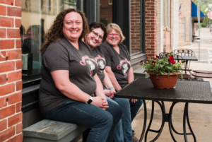 The Three Owners of CannonBelles Sit on a Bench Outside Their Storefront in Cannon Falls, MN